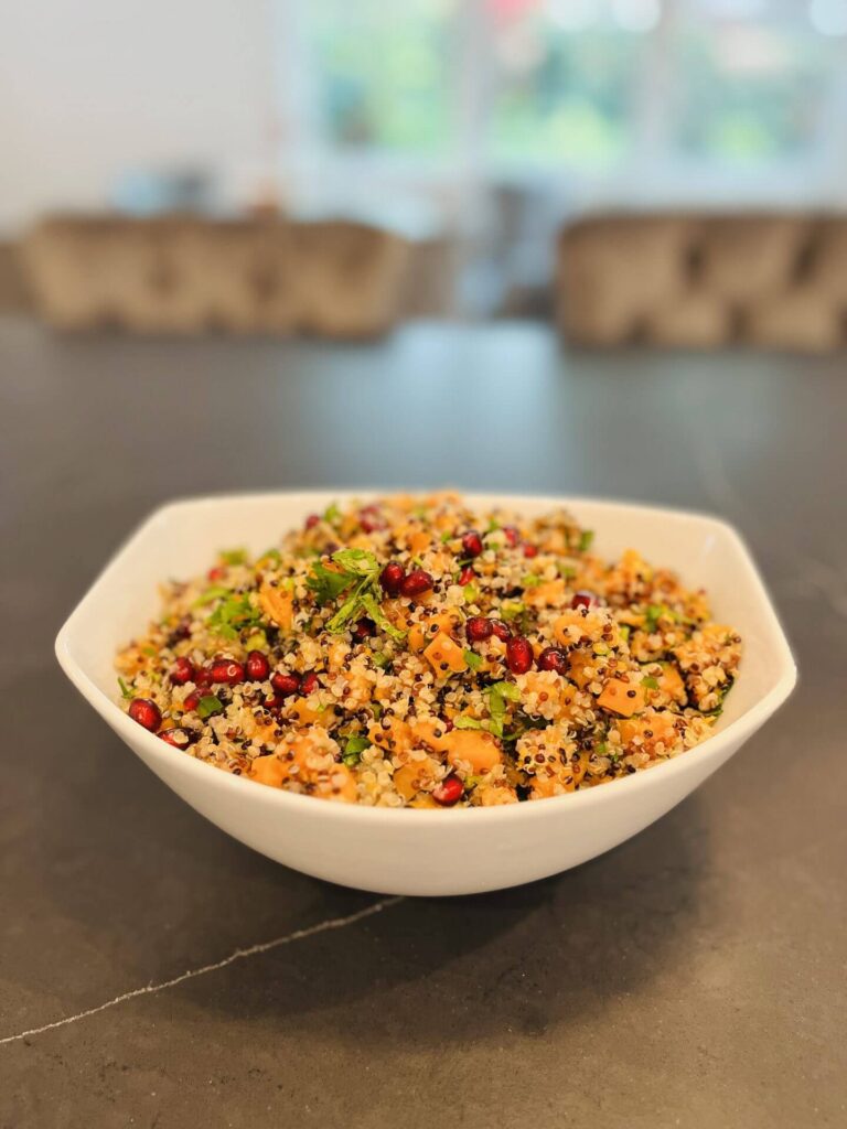Quinoa salad with roasted butternut squash, pomegranate seeds and fresh herbs in a white bowl